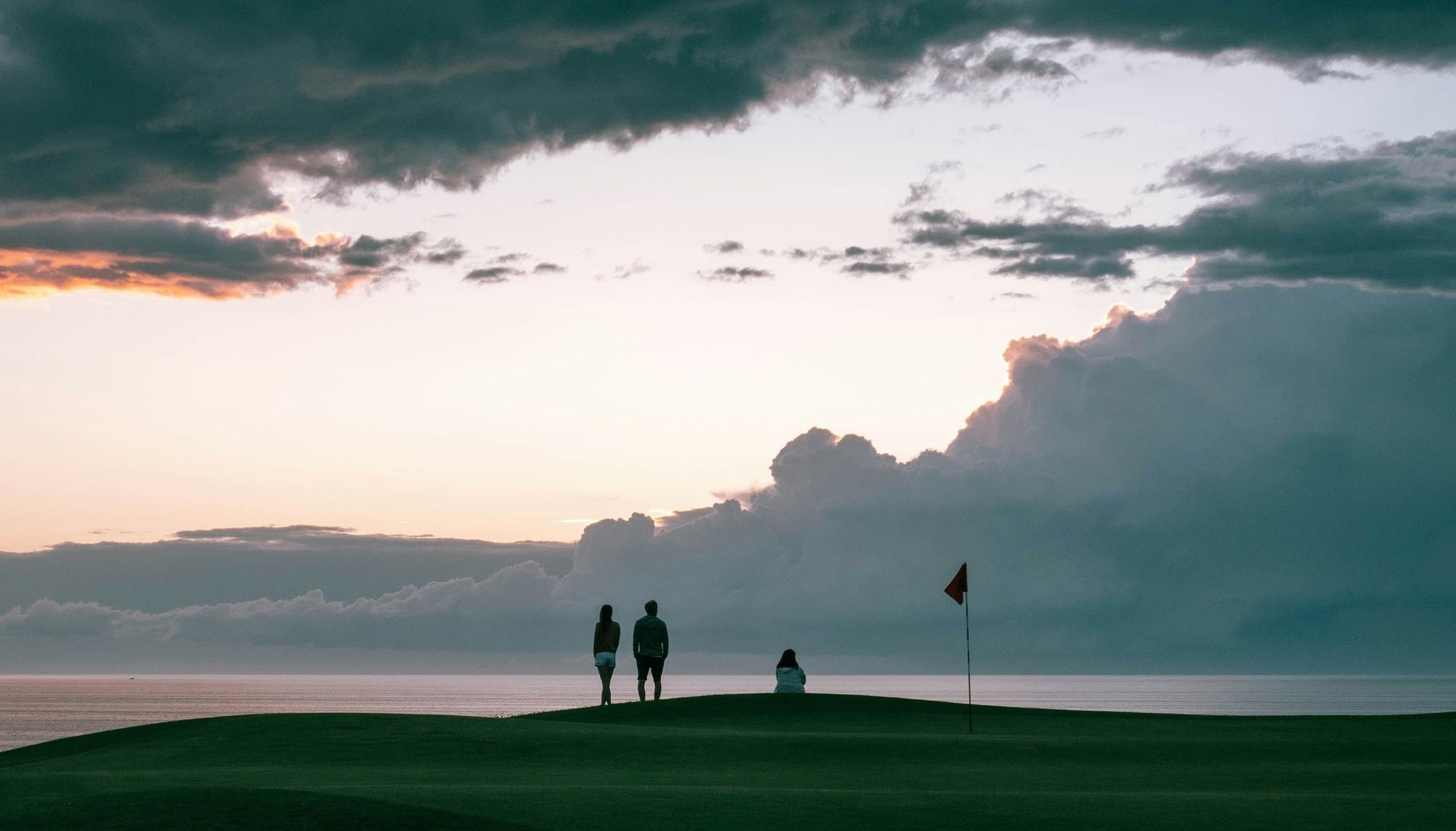 Three friends at dusk on a golf green overlooking the water, a flag beside them