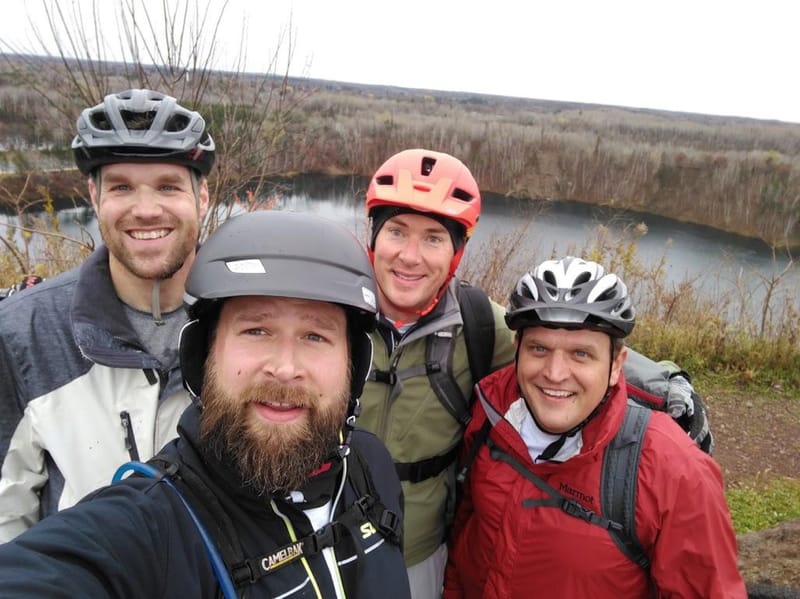 Chris Carey and three friends in bike helmets above a lake