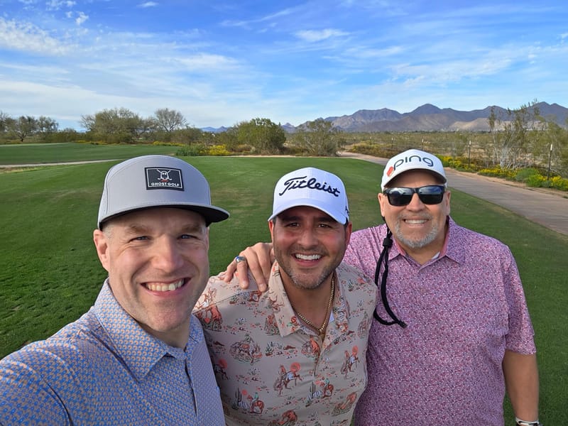 Chris Carey with two friends on a golf course, mountains behind them